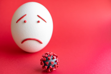 Plasticine model of coronavirus and egg isolate on a red background. Plasticine model of coronavirus and easter egg depicting fear and sadness. Large ostrich Easter egg and plasticine model of