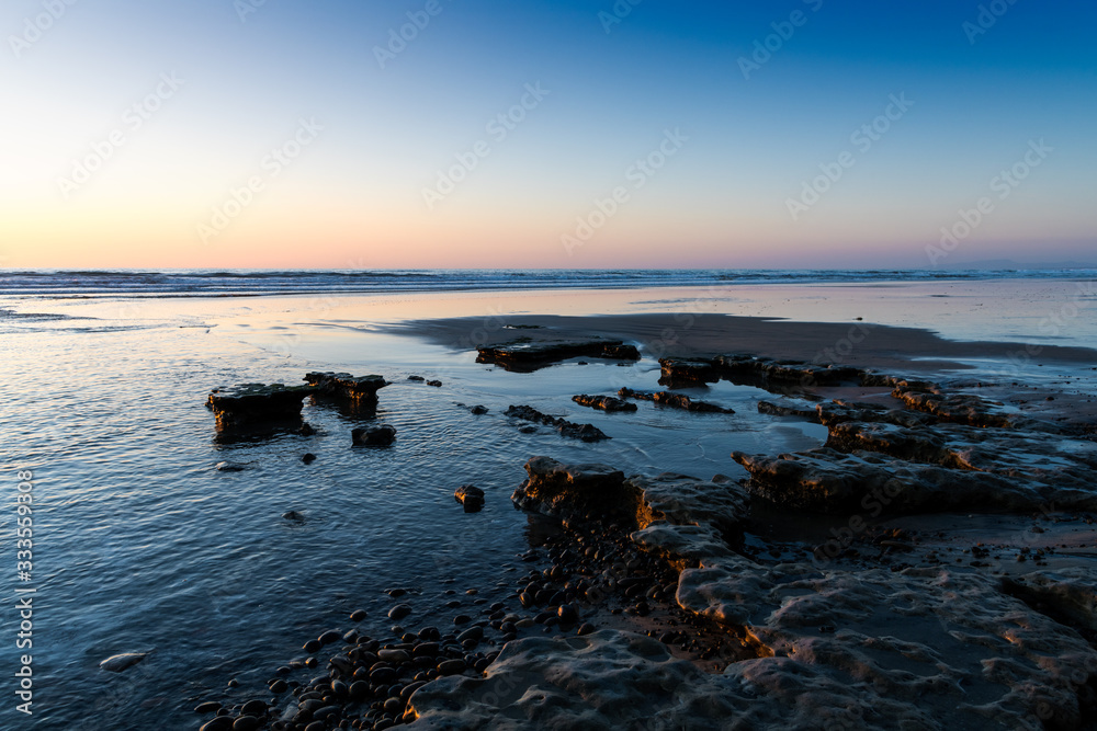 Light Beach Rocks The light of a sunset casts golden highlights in pebbles and low rock ...