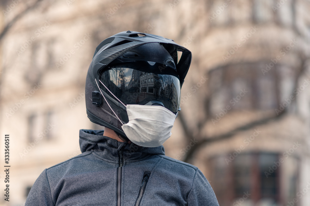 covid-19 motorcycle helmet portrait of a man in a helmet. on a motorcycle helmet a white medical mask.  photo on the street against the background of houses. coronavirus, disease,  infection, quarantine, covid-19 Stock Photo |