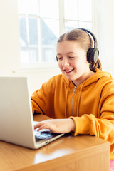 School age girl is home schooling using laptop during self isolation at her bedroom, online education, doing homework