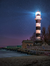 Majestyc Lighthouse With Beacon Of Light Next To Sea At Night Time Full Of Stars. 
