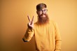 © Krakenimages.com - Handsome Irish redhead man with beard wearing glasses over yellow isolated background smiling looking to the camera showing fingers doing victory sign. Number two.
