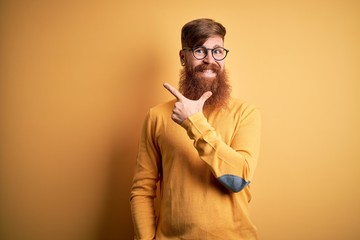 Sticker - Handsome Irish redhead man with beard wearing glasses over yellow isolated background cheerful with a smile on face pointing with hand and finger up to the side with happy and natural expression