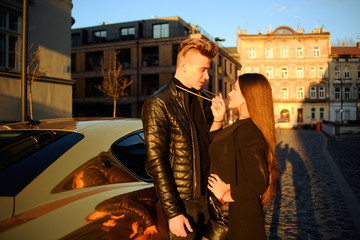 A rich couple near their cottage, and their expensive golden car. A man came to a party with a girl. Couple in black, fashion photo. A pair of glasses. Gorgeous brunette next to a rich man, success.