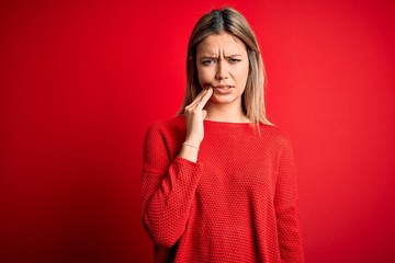 Wall Mural - Young beautiful blonde woman wearing casual sweater over red isolated background touching mouth with hand with painful expression because of toothache or dental illness on teeth. Dentist