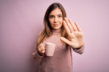 Sticker - Young blonde woman drinking a cup of coffee over pink isolated background with open hand doing stop sign with serious and confident expression, defense gesture