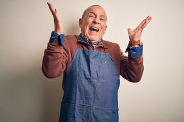 Sticker - Senior handsome baker man wearing apron standing over isolated white background celebrating mad and crazy for success with arms raised and closed eyes screaming excited. Winner concept