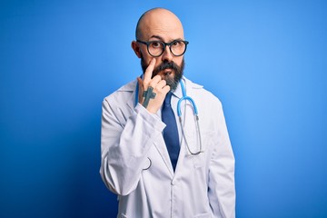 Sticker - Handsome bald doctor man with beard wearing glasses and stethoscope over blue background Pointing to the eye watching you gesture, suspicious expression