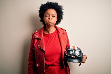 Sticker - Young African American afro motorcyclist woman with curly hair holding motorcycle helmet puffing cheeks with funny face. Mouth inflated with air, crazy expression.