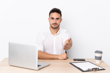 Young business man with a mobile phone in a workplace handshaking after good deal