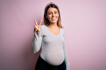 Sticker - Young beautiful brunette woman pregnant expecting baby over isolated pink background showing and pointing up with fingers number two while smiling confident and happy.