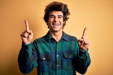 Young handsome man wearing casual shirt standing over isolated yellow background smiling confident pointing with fingers to different directions. Copy space for advertisement