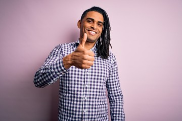 Young handsome african american afro man with dreadlocks wearing casual shirt doing happy thumbs up gesture with hand. Approving expression looking at the camera showing success.