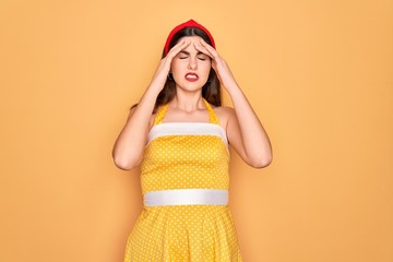 Canvas Print - Young beautiful pin up woman wearing 50s fashion vintage dress over yellow background with hand on head for pain in head because stress. Suffering migraine.