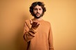 © Krakenimages.com - Young handsome man with beard wearing casual sweater standing over yellow background looking at the camera blowing a kiss with hand on air being lovely and sexy. Love expression.