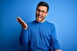 © Krakenimages.com - Young handsome man with beard wearing casual sweater and glasses over blue background smiling cheerful offering hands giving assistance and acceptance.