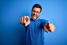 Young Handsome Man With Beard Wearing Casual Sweater And Glasses Over Blue Background Pointing To You And The Camera With Fingers, Smiling Positive And Cheerful