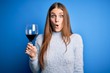 © Krakenimages.com - Young beautiful redhead woman drinking glass of red wine over isolated blue background scared in shock with a surprise face, afraid and excited with fear expression