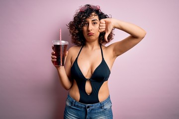 Sticker - Beautiful arab woman on vacation wearing swimsuit drinking cola refreshment using straw with angry face, negative sign showing dislike with thumbs down, rejection concept