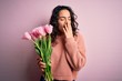Young beautiful romantic woman with curly hair holding bouquet of pink tulips bored yawning tired covering mouth with hand. Restless and sleepiness.