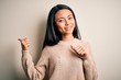 © Krakenimages.com - Young beautiful chinese woman wearing casual sweater over isolated white background Pointing to the back behind with hand and thumbs up, smiling confident