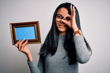 Wall Mural - Young beautiful chinese woman holding vintage frame over isolated white background with happy face smiling doing ok sign with hand on eye looking through fingers