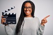 Young african american director girl filming a movie using clapboard over isolated background very happy pointing with hand and finger to the side