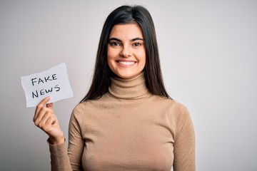 Young beautiful brunette woman holding paper with fake news message over white background with a happy face standing and smiling with a confident smile showing teeth