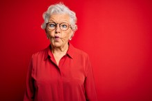 Senior Beautiful Grey-haired Woman Wearing Casual Shirt And Glasses Over Red Background Making Fish Face With Lips, Crazy And Comical Gesture. Funny Expression.