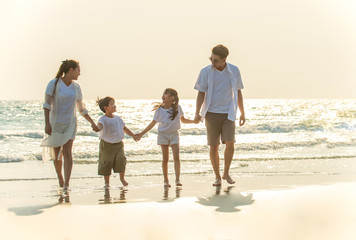 Smiling Young Asian happy family parents with child walking and holding hands together on the beach in summertime. Father, mother and kids relax and having fun summer lifestyle travel holiday vacation