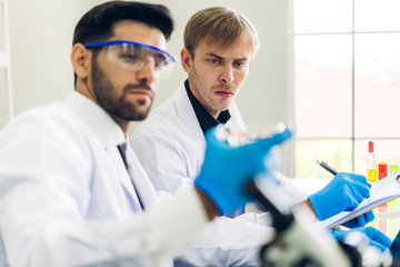 Professional two scientist man research and working doing a chemical experiment while making analyzing and mixing  liquid in test tube.Young science man dropping sample chemical on glass at laboratory