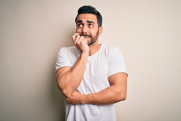 Canvas Print - Young handsome man with beard wearing casual t-shirt standing over white background looking stressed and nervous with hands on mouth biting nails. Anxiety problem.