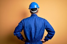 Mechanic Man With Beard Wearing Blue Uniform And Safety Helmet Over Yellow Background Standing Backwards Looking Away With Arms On Body