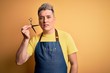 © Krakenimages.com - Young handsome blonde hairdresser man wearing apron holding scissors standing over isolated yellow background
