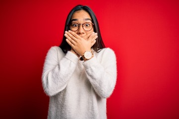 Sticker - Young beautiful asian woman wearing casual sweater and glasses over red background shocked covering mouth with hands for mistake. Secret concept.