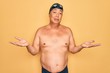 © Krakenimages.com - Middle age senior grey-haired swimmer man wearing swimsuit, cap and goggles clueless and confused with open arms, no idea concept.