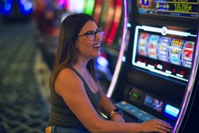 Young Beautiful Woman Smiling Happy And Confident. Sitting With Smile On Face Playing Slot Machine At Casino