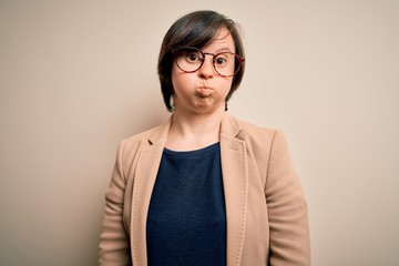 Wall Mural - Young down syndrome business woman wearing glasses standing over isolated background puffing cheeks with funny face. Mouth inflated with air, crazy expression.