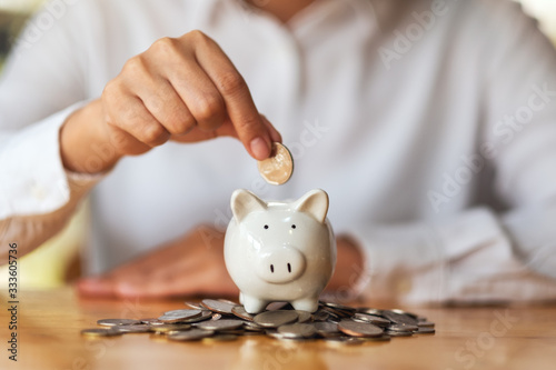 Fotografía A woman putting coins into piggy bank on pile of coins on the table for saving m