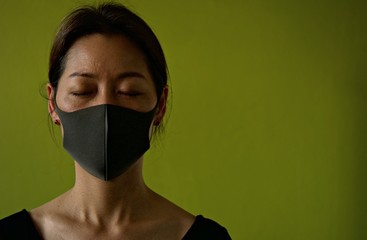 Asian woman wearing facial mask for protection from air pollution or virus epidemic on dark green background, she worried about Covid-19 situations.