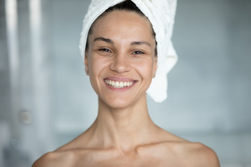 Wall Mural - Head shot portrait excited beautiful woman with healthy perfect skin toothy smile after shower posing in bathroom head wrapped in towel looking at camera. Concept of natural beauty skin and body care