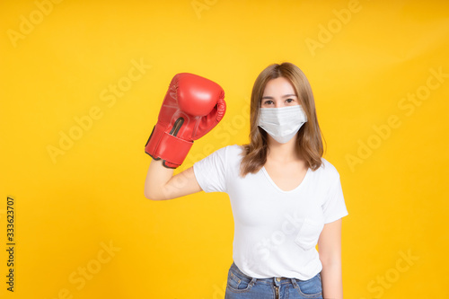 Young asian woman with medical mask protection coronavirus COVID-19 fighting wearing boxing gloves healthy and safety care concept on yellow background isolated studio shot, copy space Poster Mural XXL