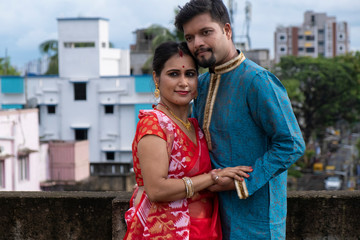 A brunette Indian Bengali romantic couple in traditional wear enjoying themselves standing on the roof top in sunny morning of Durga Puja festival in green natural background. Indian lifestyle.