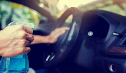 Hand of driver is spraying alcohol to car steering wheel to kill the Coronavirus Covid19 or contamination of germ. Driver is cleaning and wipe surfaces that are frequently touch with spraying alcohol.