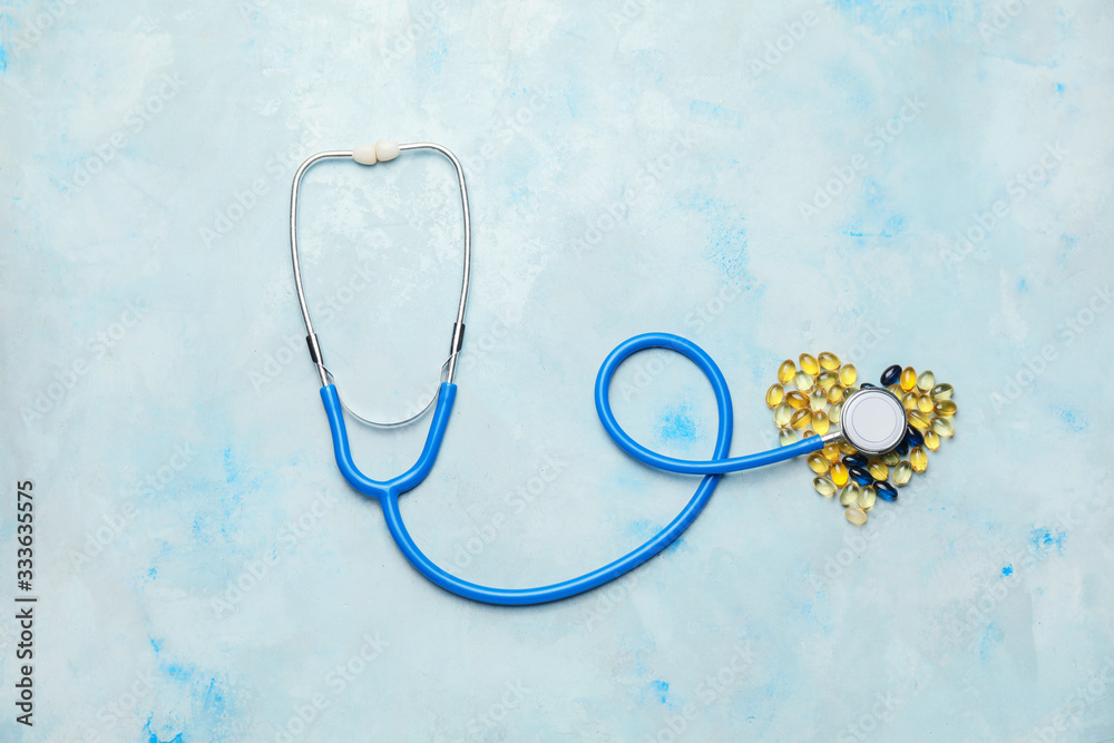 Heart made of pills and stethoscope on color background