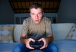 © TheVisualsYouNeed - young excited and concentrated man at home playing videogames holding controller looking stressed and focused in video gaming addiction and technology geek concept