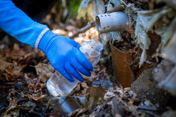 Ecologist taking water samples from a natural source in protective gloves