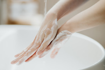 Closeup of a woman washing her hands in bathroom to prevent Covid-19 viral infection. Recommended washing with soap and running water during coronavirus pandemic.