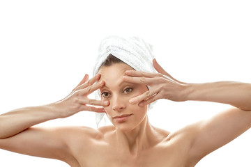 Facial massage at home. Massage the skin around the eyes. Wrinkle smoothing. Beautiful young woman with a white towel on her head and with clean perfect skin. Isolated white background.