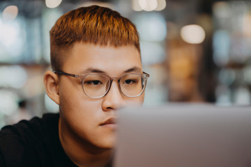 Asian young man indoors in cafe. Lifestyle concept photo with copy space. Picture with handsome guy who using protective face mask. Portrait with gray laptop
